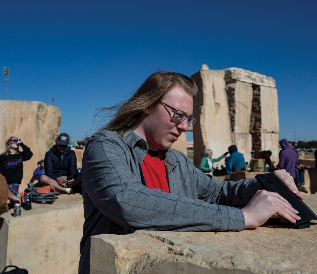 A person balances their phone on a rock while pointing it at the sky.