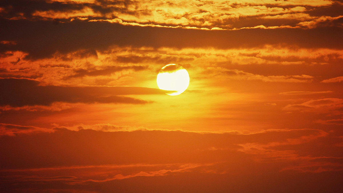 Un Sol anaranjado se eleva sobre un banco de nubes.