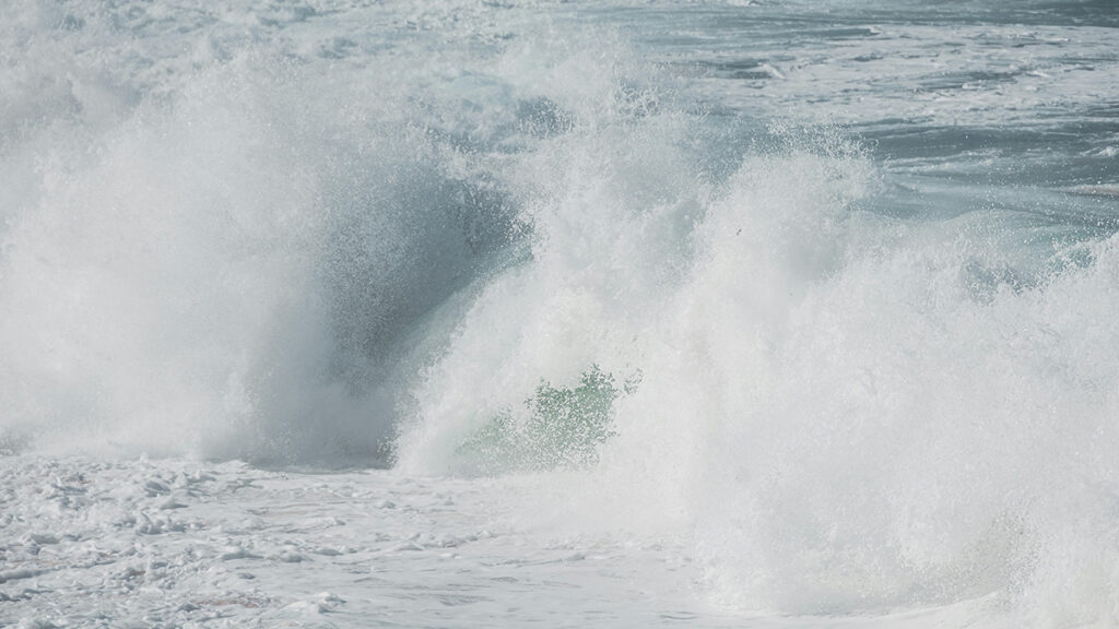 Ocean waves crash, releasing water droplets into the air.