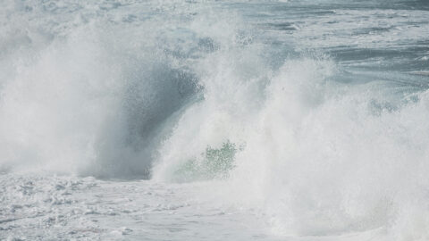 Ocean waves crash, releasing water droplets into the air.
