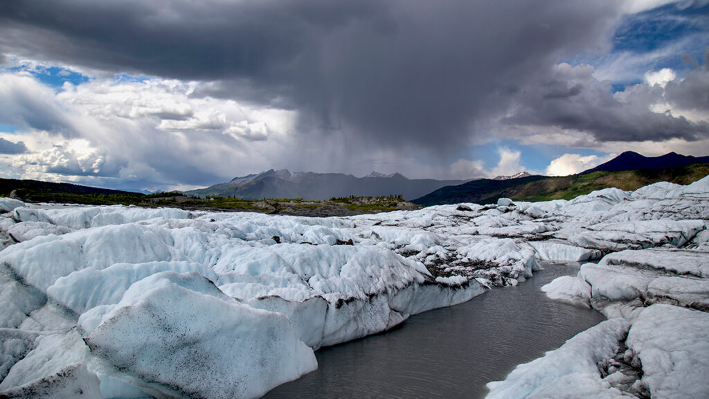 Floating ice is seen in the foreground, and an ominous storm cloud lies over a distant mountain range.