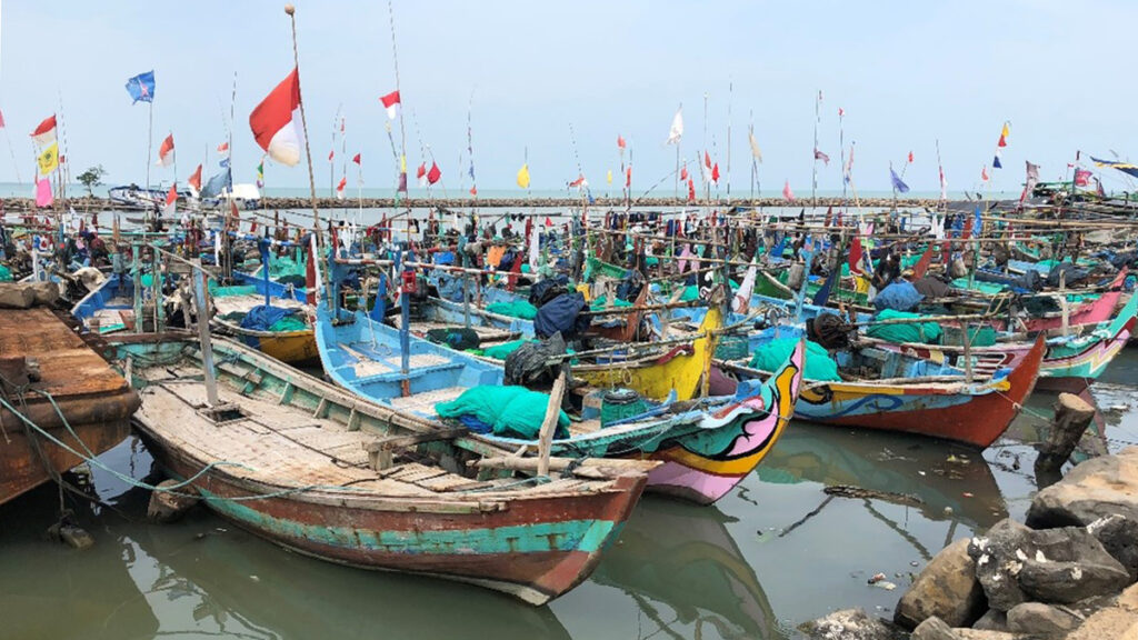 A fleet of small, colorfully painted fishing boats adorned with flags sits in the water at a dock.