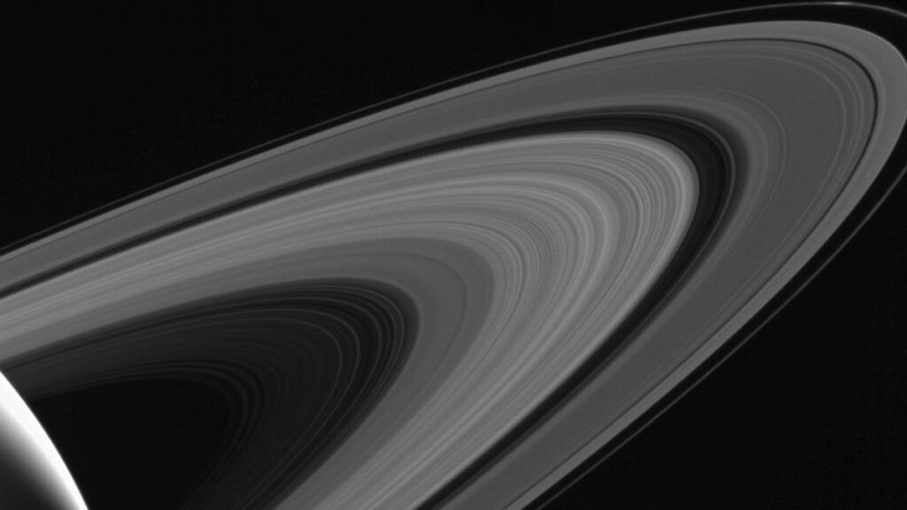 A series of curved lines, some brighter than others, encircle a planet that’s partially visible in the lower left foreground.