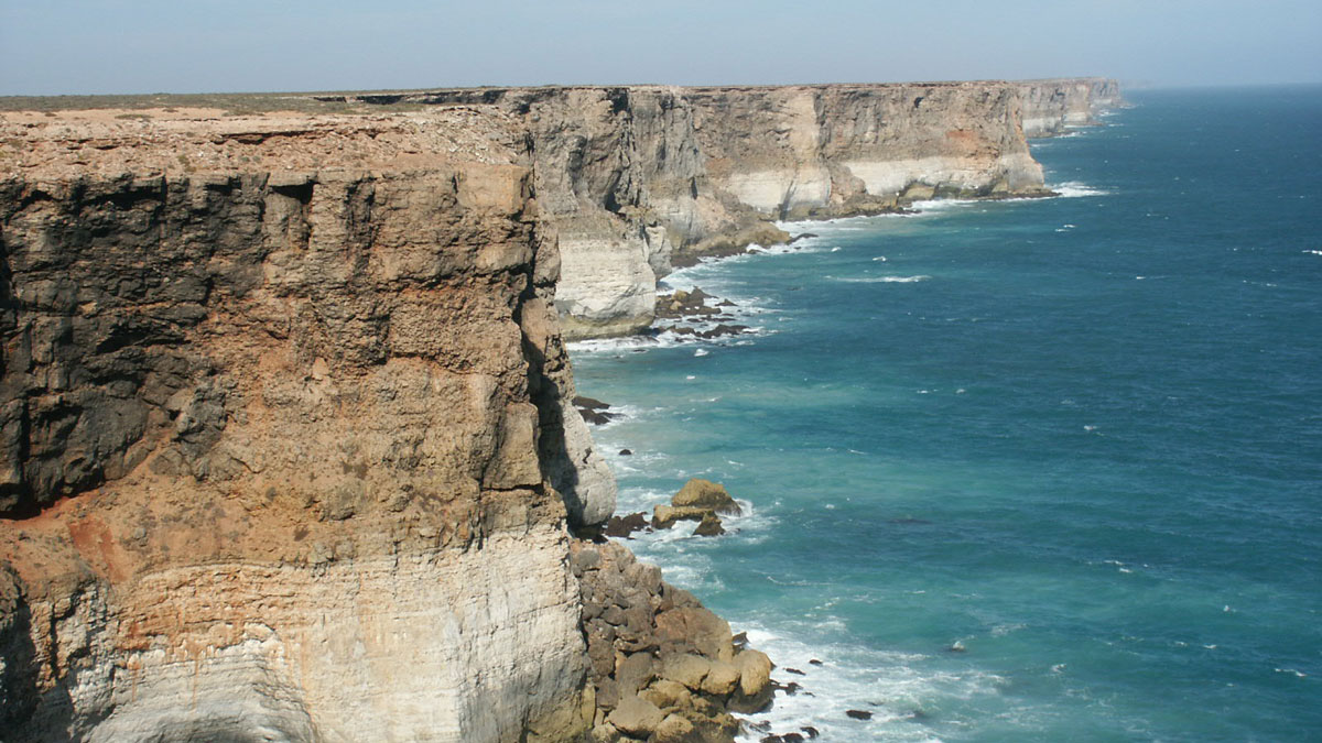 Acantilados grises y beige a la izquierda con vistas a un océano azul a la derecha.
