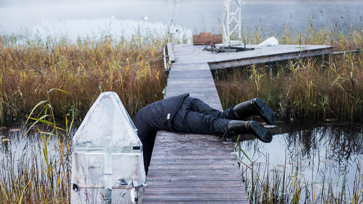 A scientist leans off a dock to sample methane emissions from a lake in Sweden.