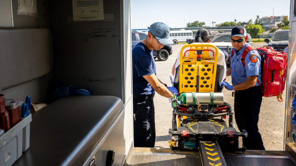 A photo taken from inside an ambulance of a paramedic moving a stretcher into the vehicle.