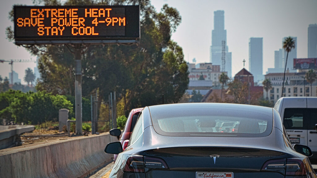 Cars next to an electronic highway sign with an extreme heat warning