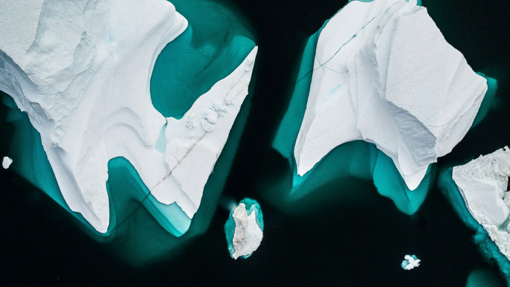White and bright blue icebergs against a dark blue ocean photographed from above.