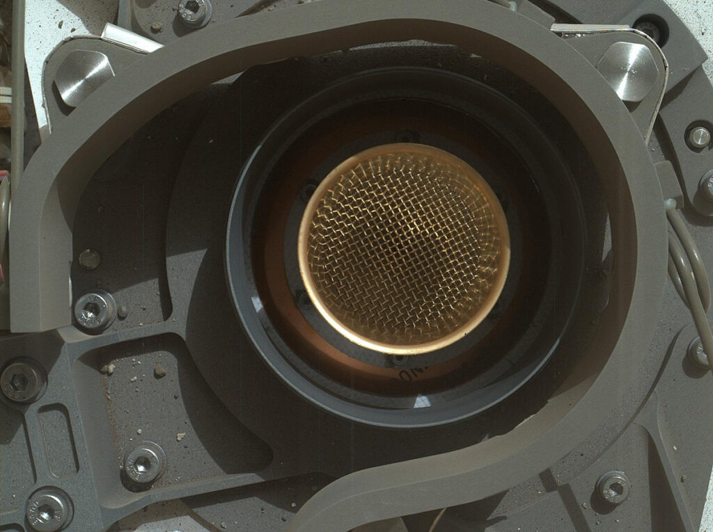 A round screen that is part of a scientific instrument sits atop the Curiosity rover on Mars.