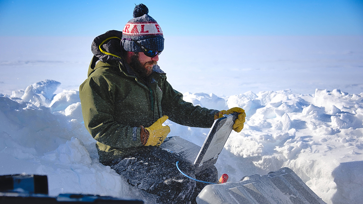 Researcher Matthew R. Siegfried uses a laptop in a frigid, if sunny, Antarctic landscape.