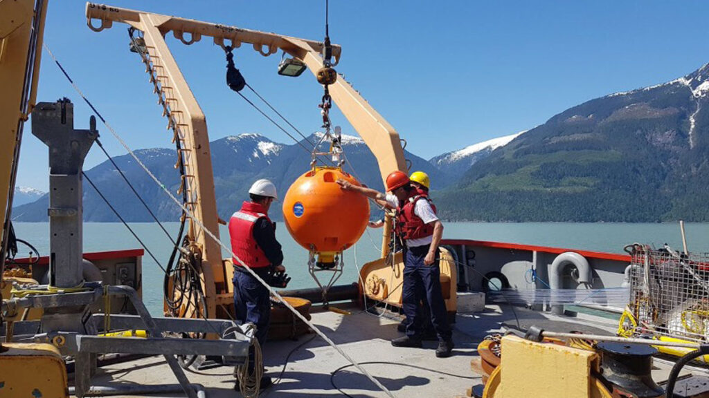 A photo of a large orange buoy on a boat with several people gathered around it