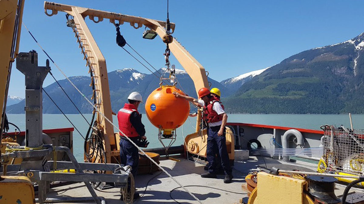 A photo of a large orange buoy on a boat with several people gathered around it