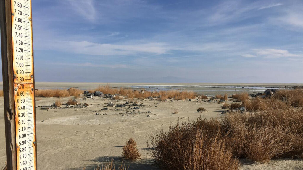 A gauge used to measure lake levels stands on a dry, sandy lake bed