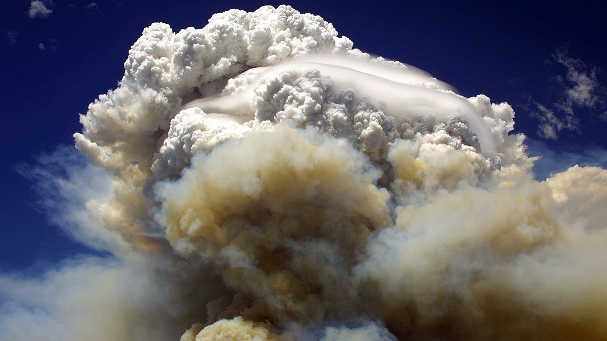 A brown plume of smoke leads to a tall, white popcorn-looking cloud.