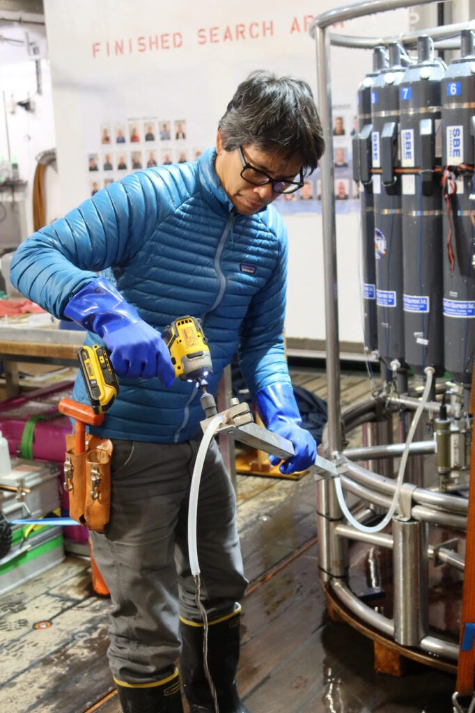 David Ho takes a water sample from a hose attached to cylinders in the background.