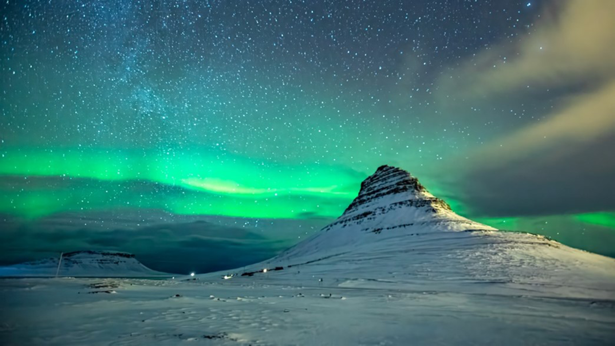 Photo of a mountain at night with an aurora and stars in the background.
