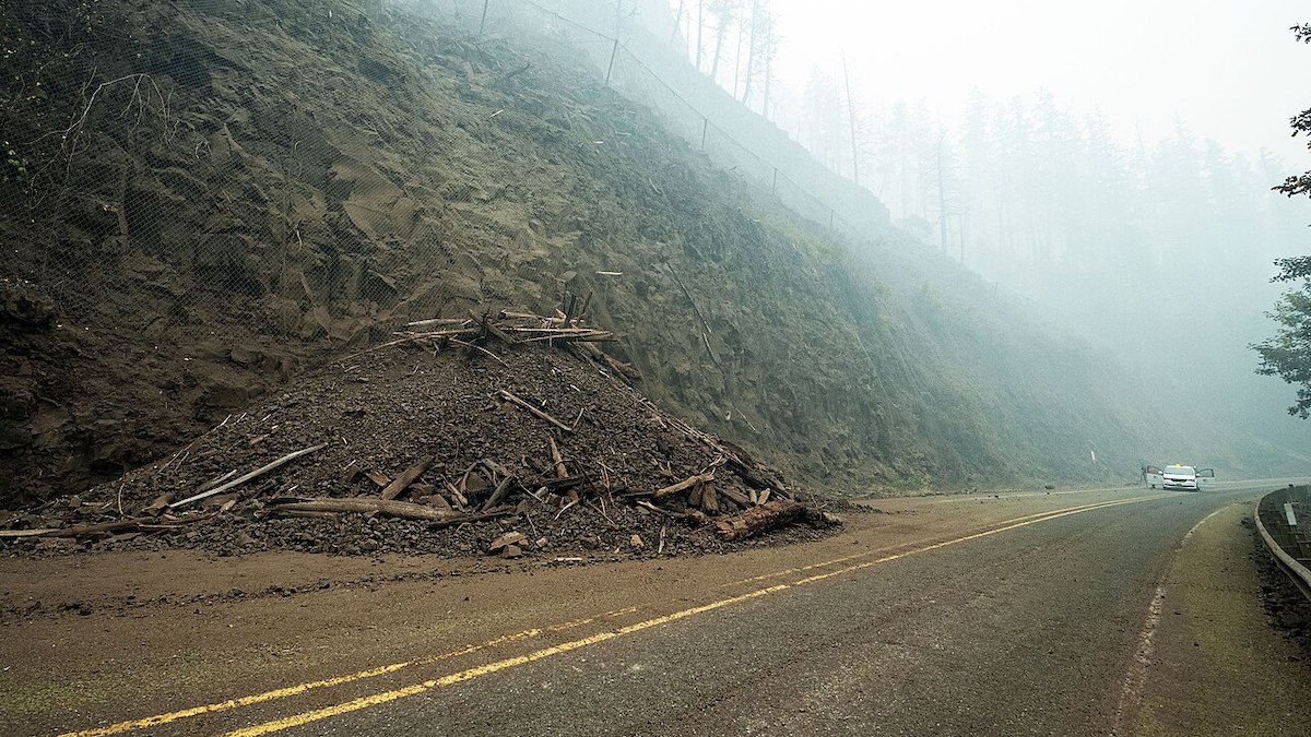 Dirt, rocks, and tree debris block one lane of a mountain highway.