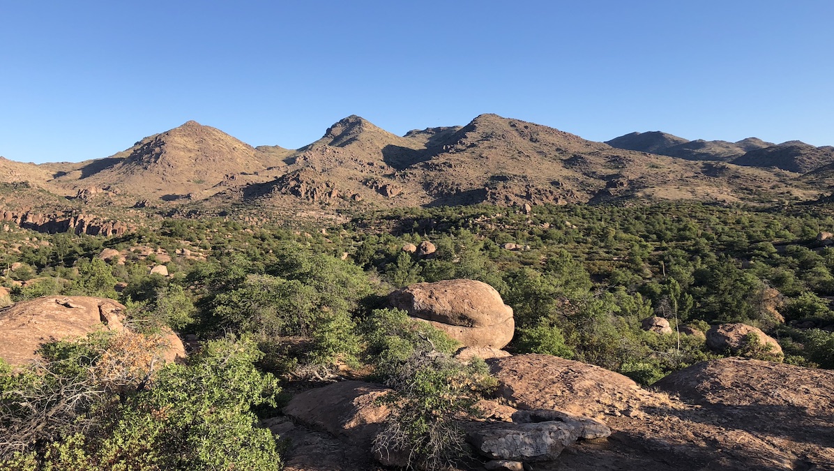 A photo depicts a landscape with three large hills in the background and rocks and shrubs in the foreground.