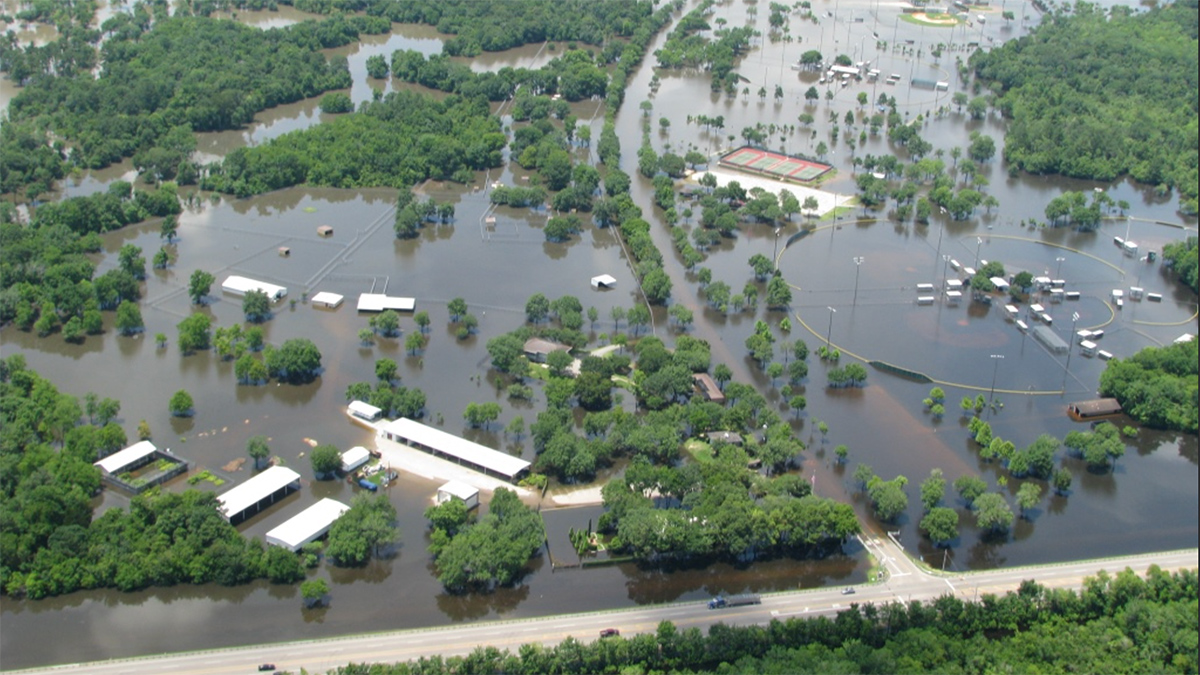 Aerial view of a flooded area, where ponded water has filled in all low-lying areas, and some roads. Trees and buildings are sticking up out of the water.