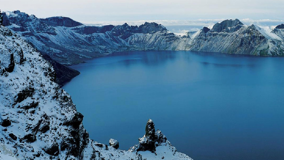 A strikingly blue lake surrounded by the snowcapped rock walls of a volcano.