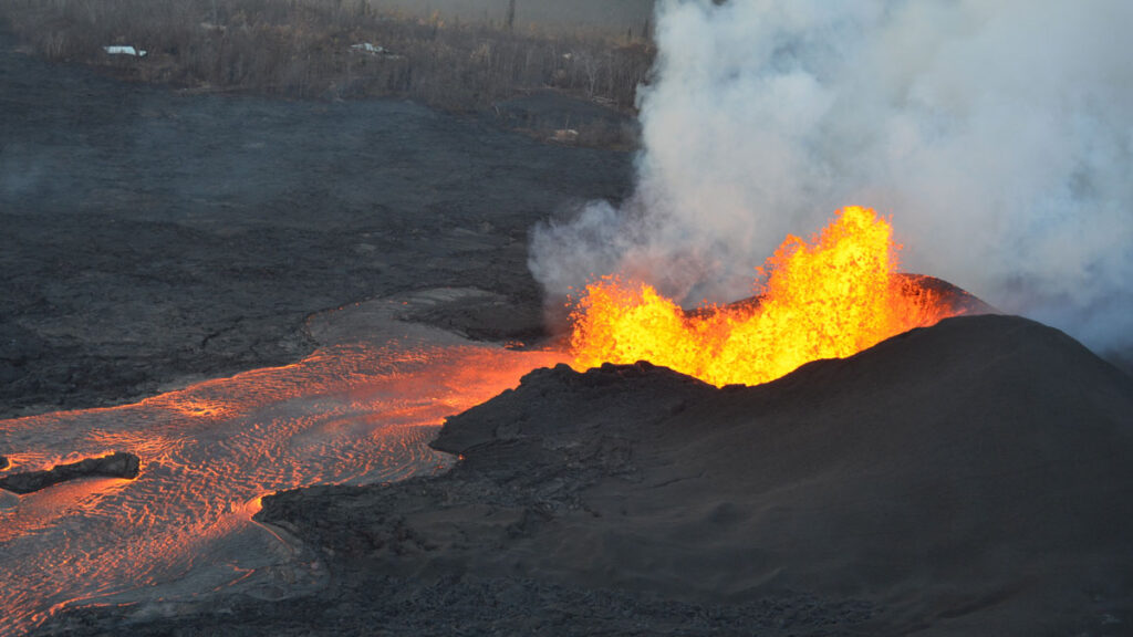 Orange and yellow lava shoots out of a black mound.