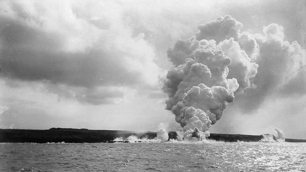A volcanic eruption near the ocean sends smoke and steam into the sky.