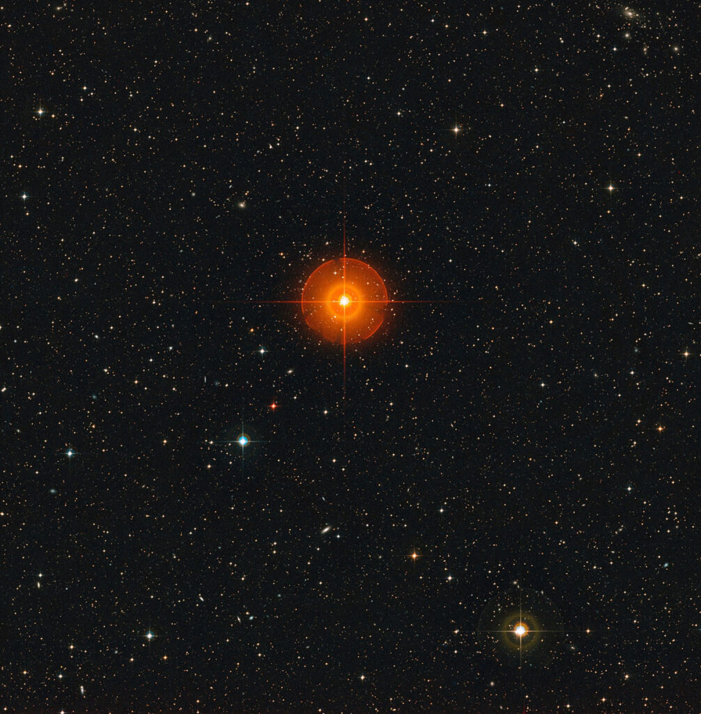 A bright orange star is surrounded by an orange halo, with several other bright stars in the background.