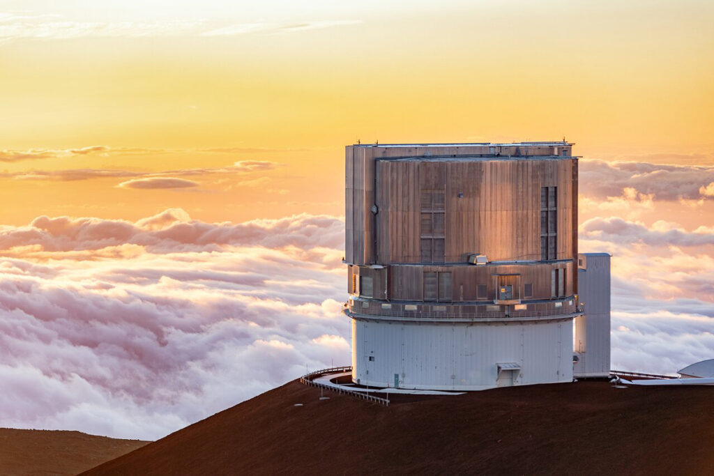 A cylinder-shaped building on a mountain above clouds in yellow light