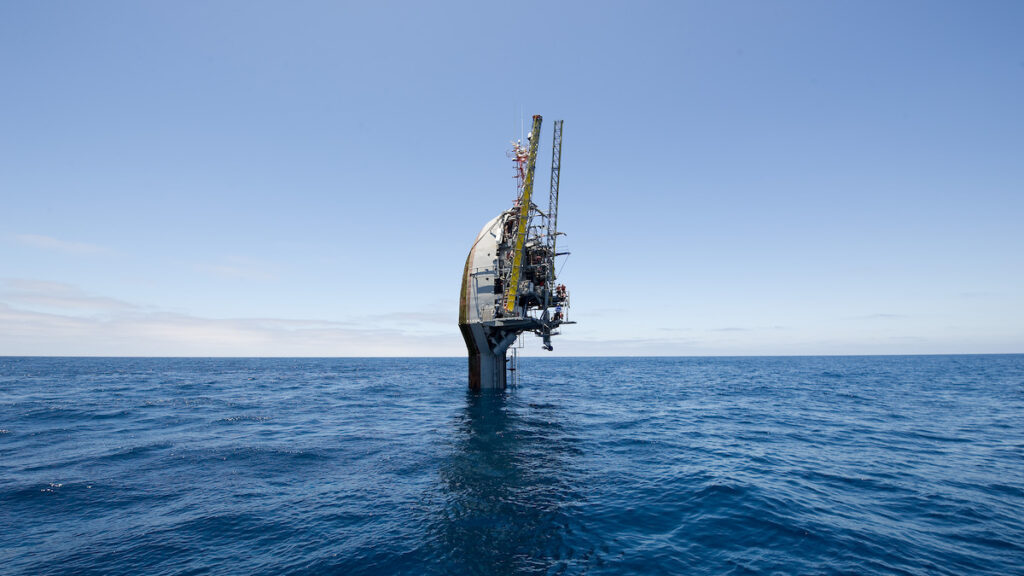 Research vessel FLIP, in its vertical position, floats in the ocean. It looks like the head of a spoon with scaffolding.