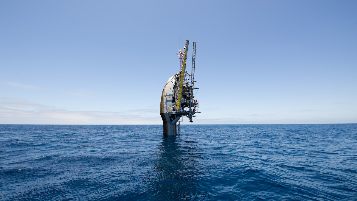 Research vessel FLIP, in its vertical position, floats in the ocean. It looks like the head of a spoon with scaffolding.