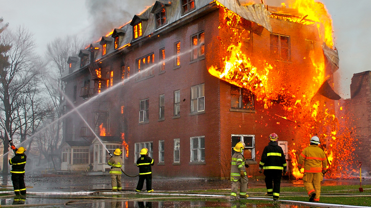 Firefighters spray water at a four-story burning brick building.