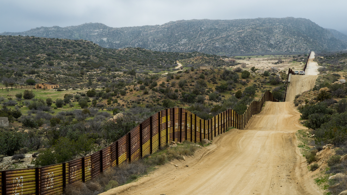 A border wall between the United States and Mexico with a dirt road alongside it