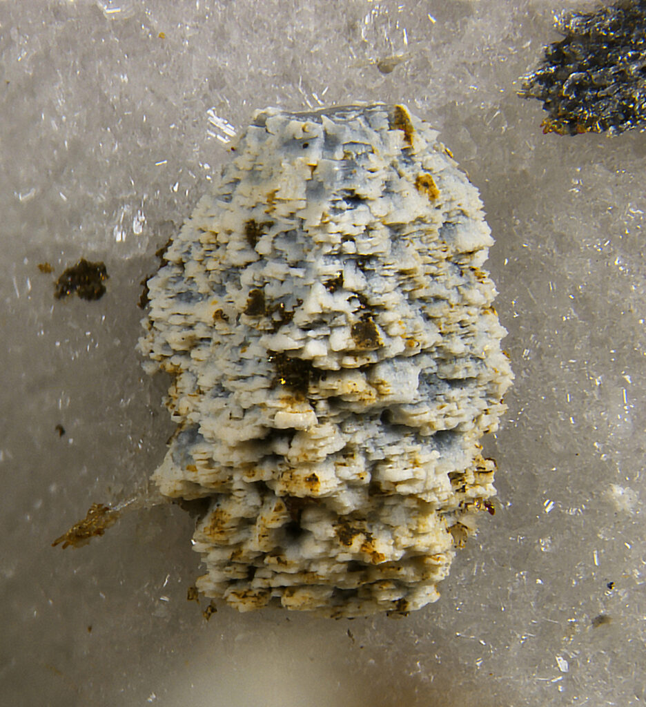 White mineral with speckles of yellowish brown on a white crystal background