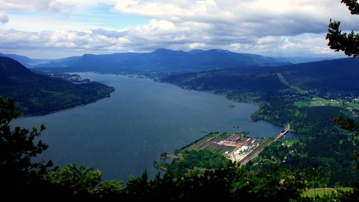 A wide, blue river is bordered on both sides by green mountains.