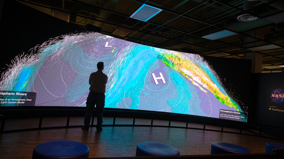 A person stands in front of a large digital display with an atmospheric river visualization.
