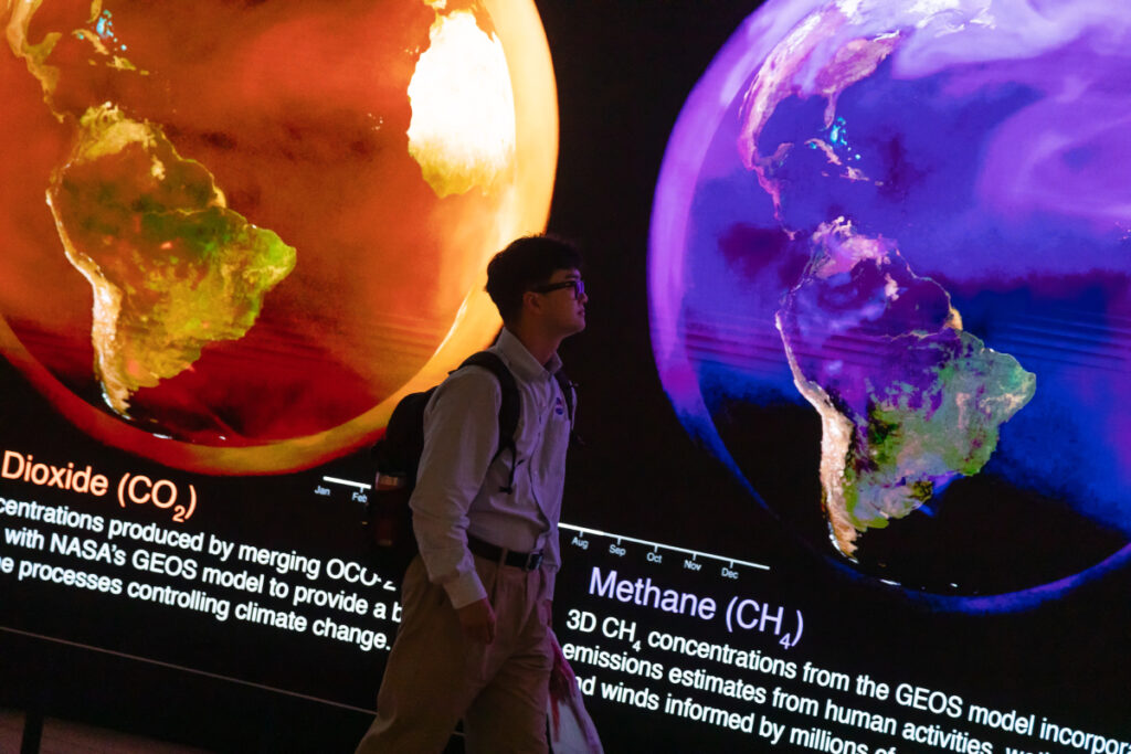 A person walks in front of a digital display with orange and purple maps of Earth.