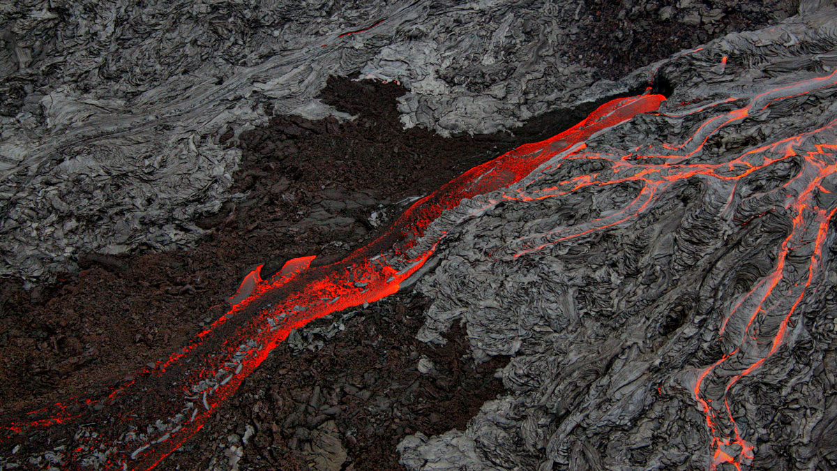 An aerial view of lava flows, some black and hardened and some molten red.
