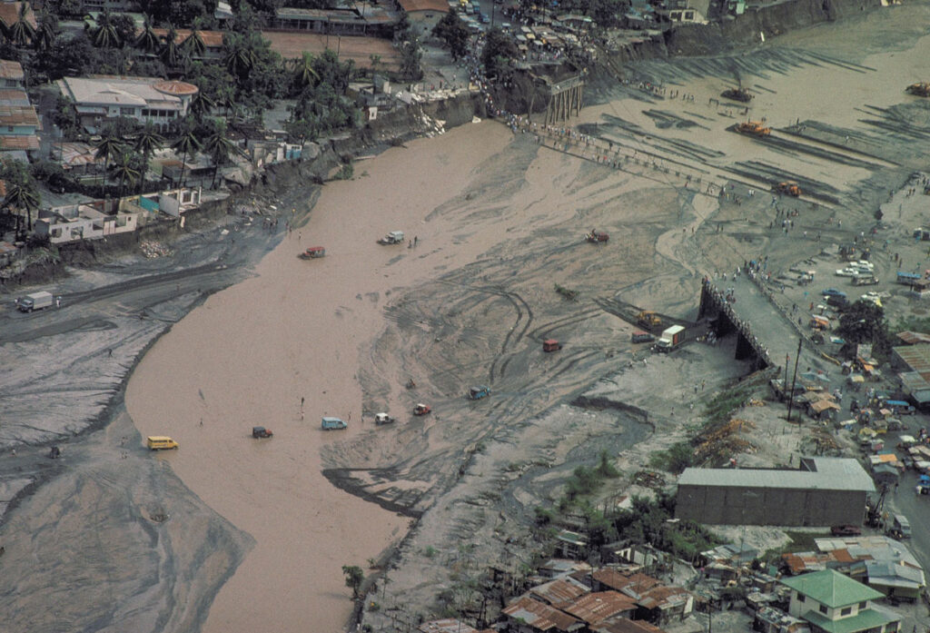 Vista aérea de vehículos y personas cruzando un canal de río fangoso cerca de donde un puente fue arrasado.