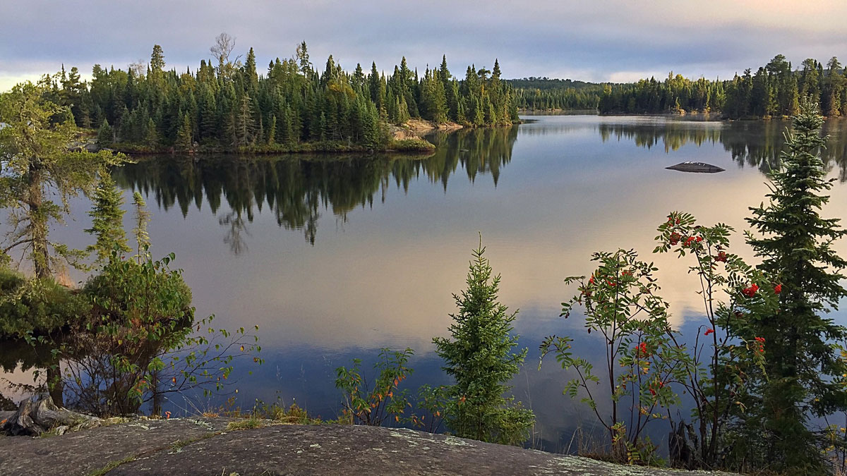A calm lake is surrounded by evergreen trees that reflect in its waters.