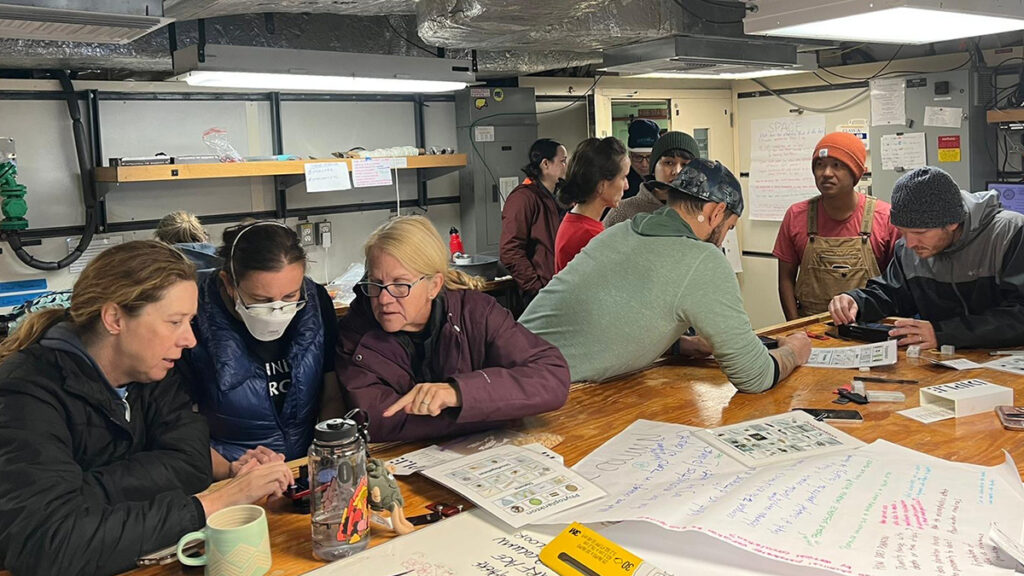 Los participantes en un crucero de investigación para profesores de colegios de dos años utilizan lentes de microscopio acoplados a teléfonos inteligentes para observar muestras de plancton sobre una mesa en un laboratorio a bordo de un buque de investigación.