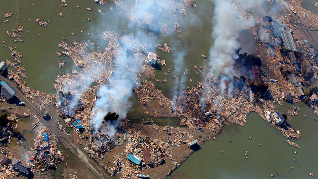An aerial image shows ruins of buildings and smoke after the 2011 Tohoku earthquake.