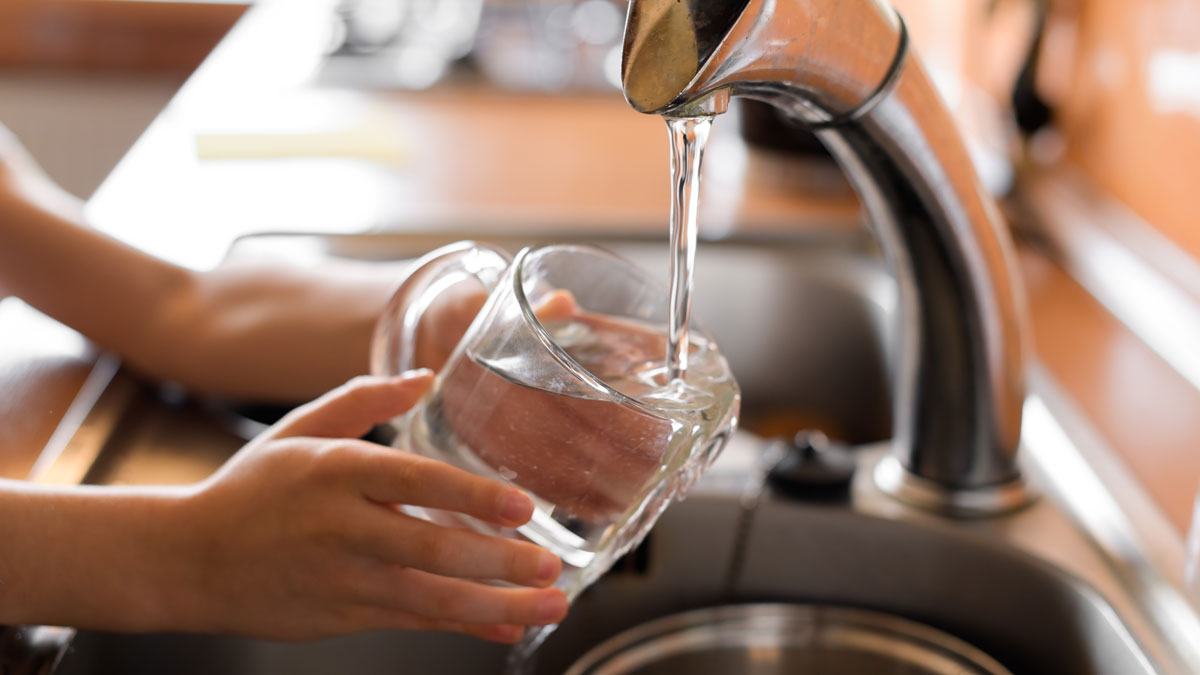 Small hands hold a clear glass under a kitchen faucet and fill it with water.
