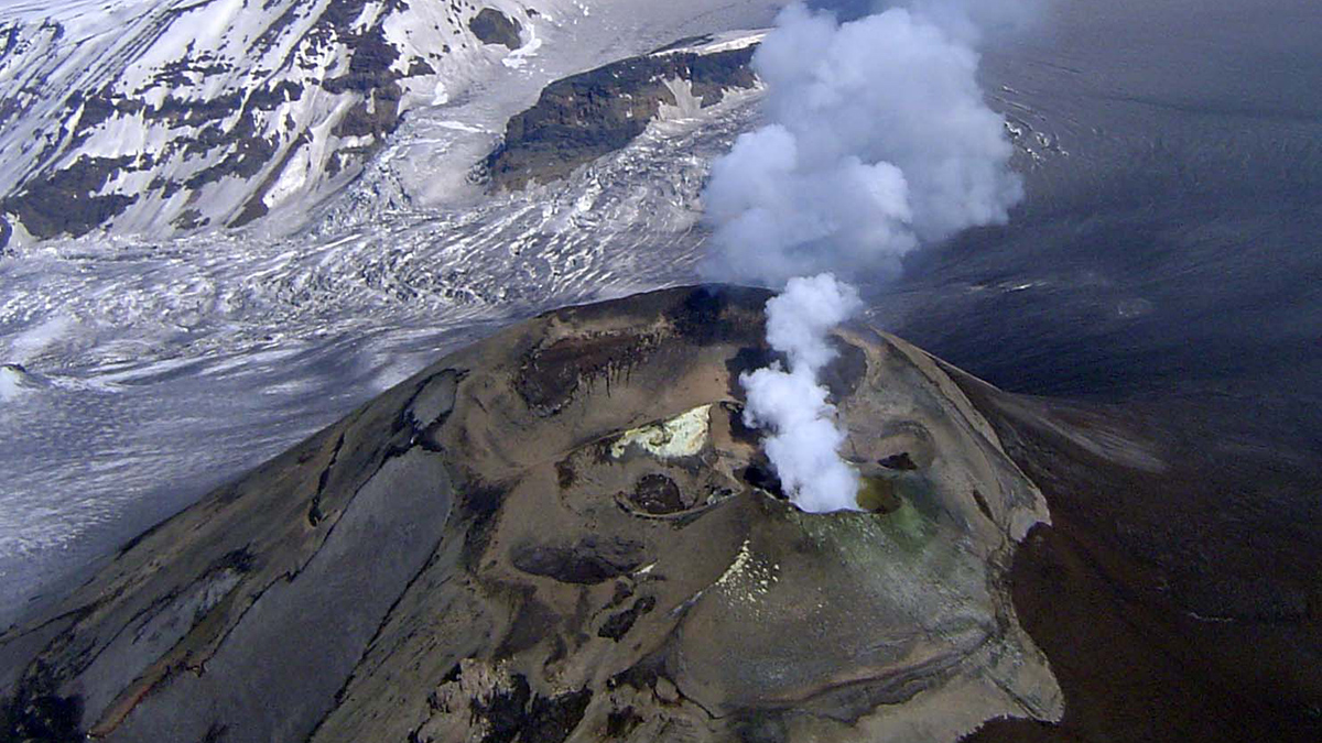 Volcanic eruption with steam rising from a snow-covered peak.