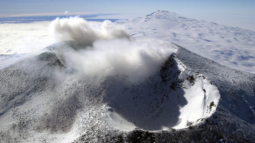The crater of a snow-covered volcano emits smoke.