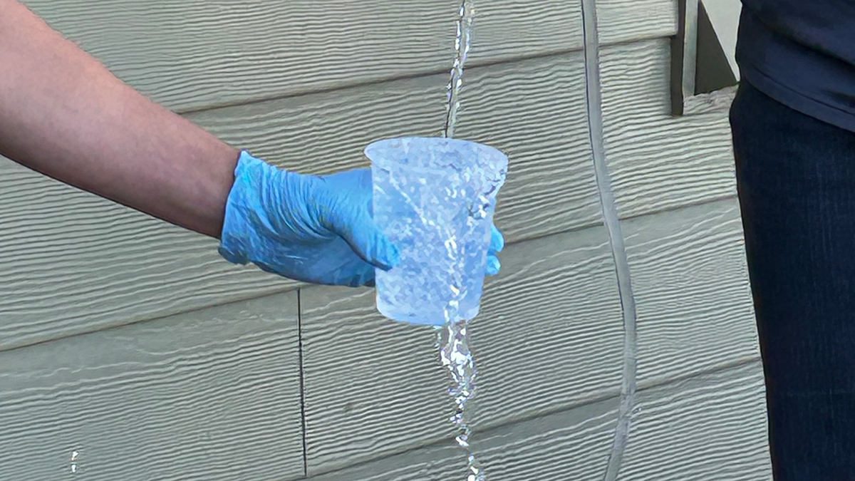 A hand in a blue glove holds a plastic cup out to catch a stream of water.