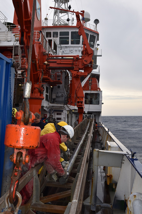 People in helmets bend over equipment near the side of a boat.