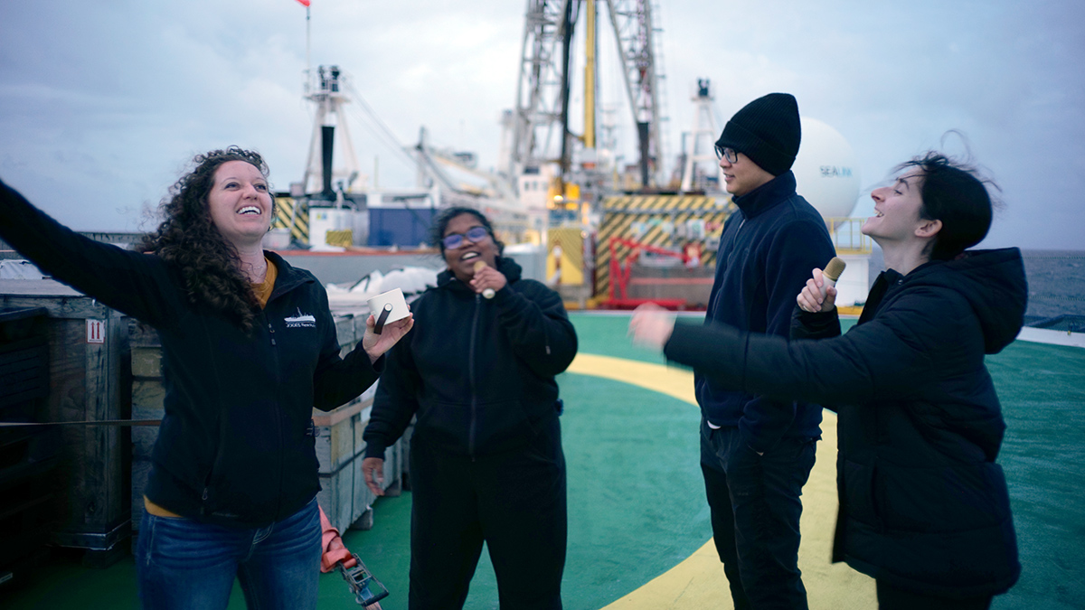 Four scientists celebrate with karaoke on the deck of the JOIDES Resolution.