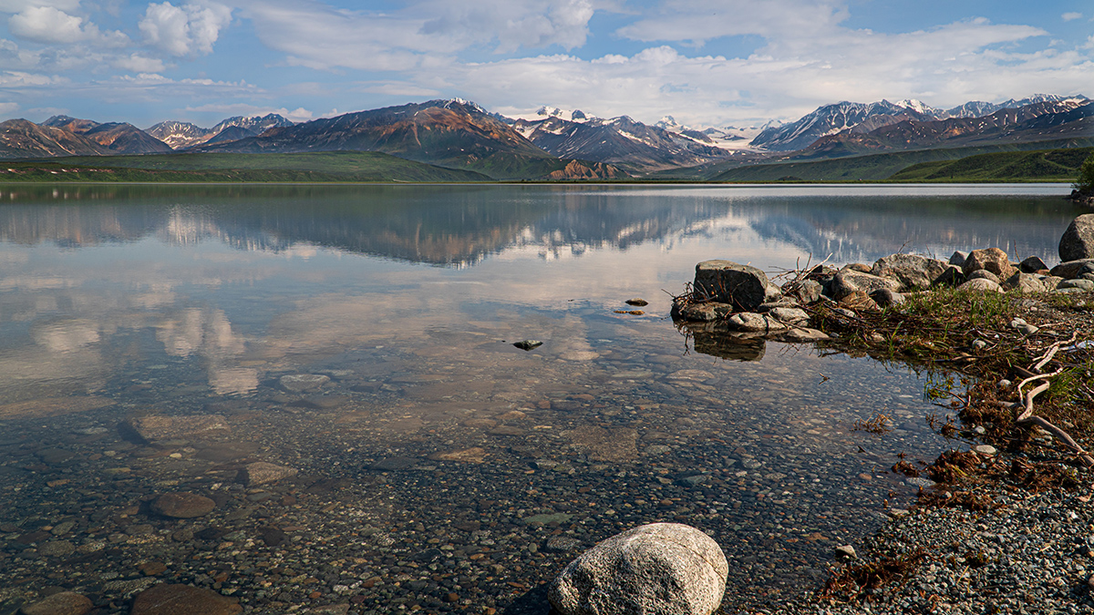 A mountain, glacier, and blue sky are reflected in the surface of a calm lake.