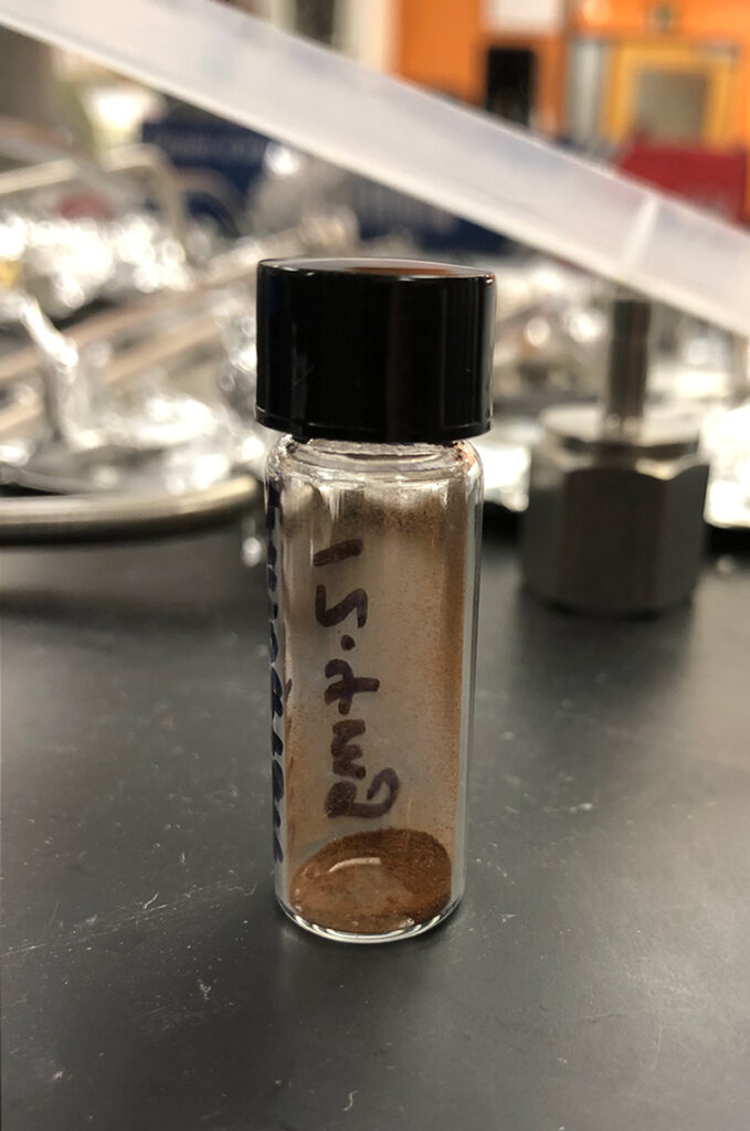A small glass tube with a black plastic stopper, containing red-brown powder