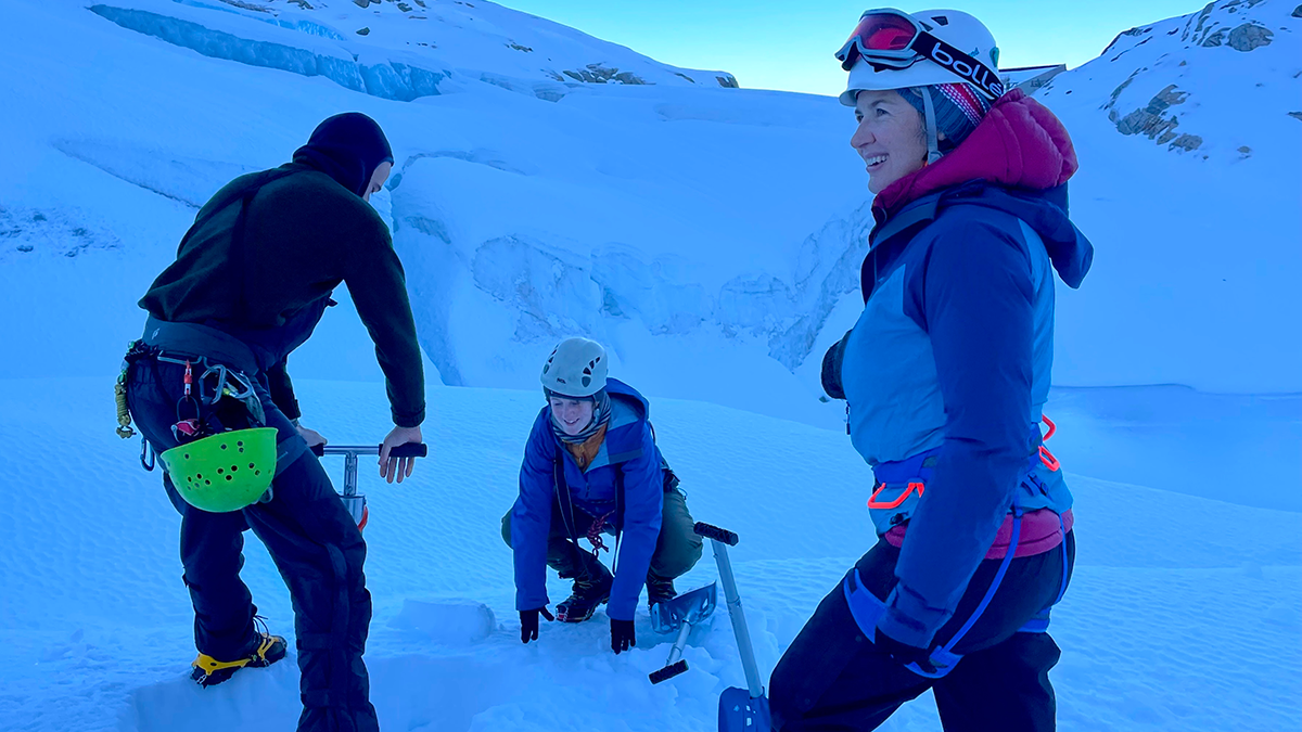 Photo of 3 scientists doing field work on a glacier.
